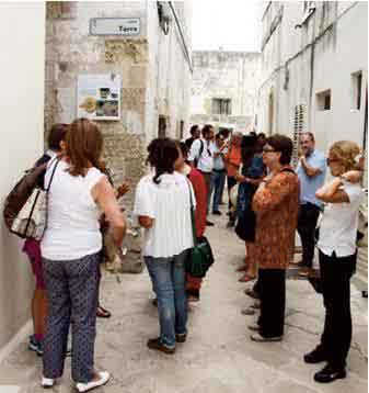 persone ascoltano la descrizione  di un pannello didascalico nel centro storico di Muro Leccese