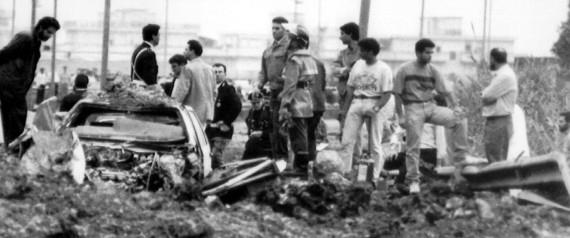 Foto in bianco e nero di uomini su luogo della strage con auto distrutta
