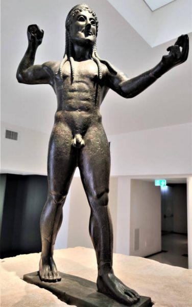 Statua in pietra nera di uomo nudo con capelli lunghi con trecce