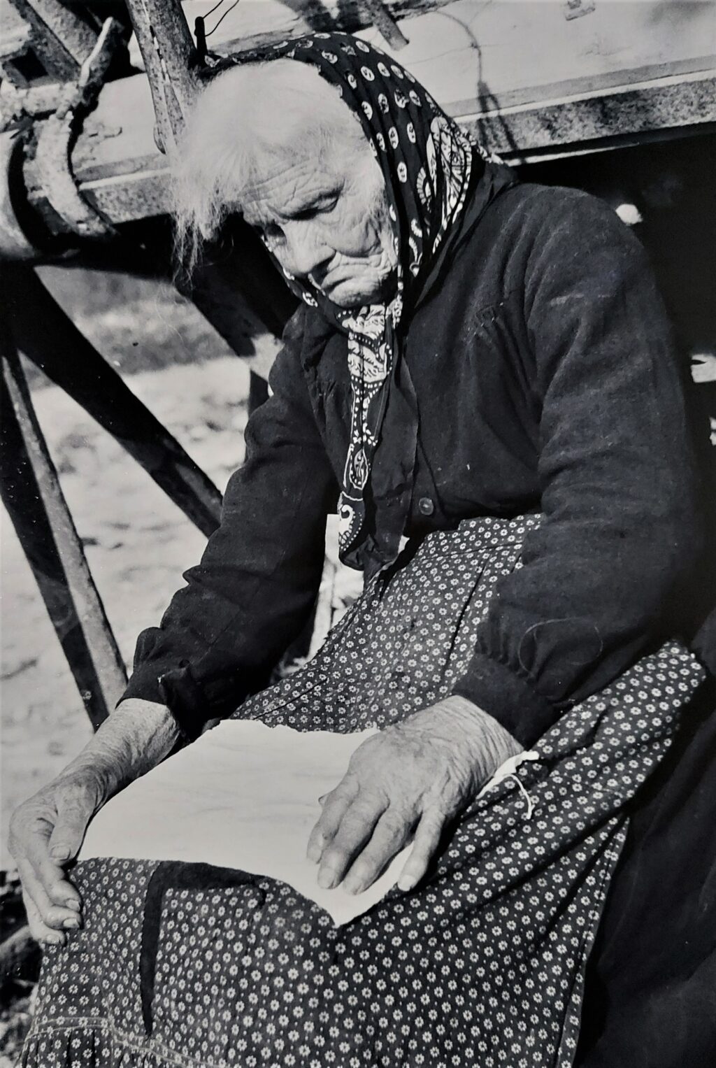 La foto ritrae una vecchia signora seduta che osserva un fazzoletto aperto sulle sue ginocchia
